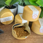 Gold containers with tea powder on a wooden surface with plants in the background