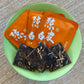 Three fanned orange envelopes beside three fanned white tea cakes with pressed-in orange peel slices