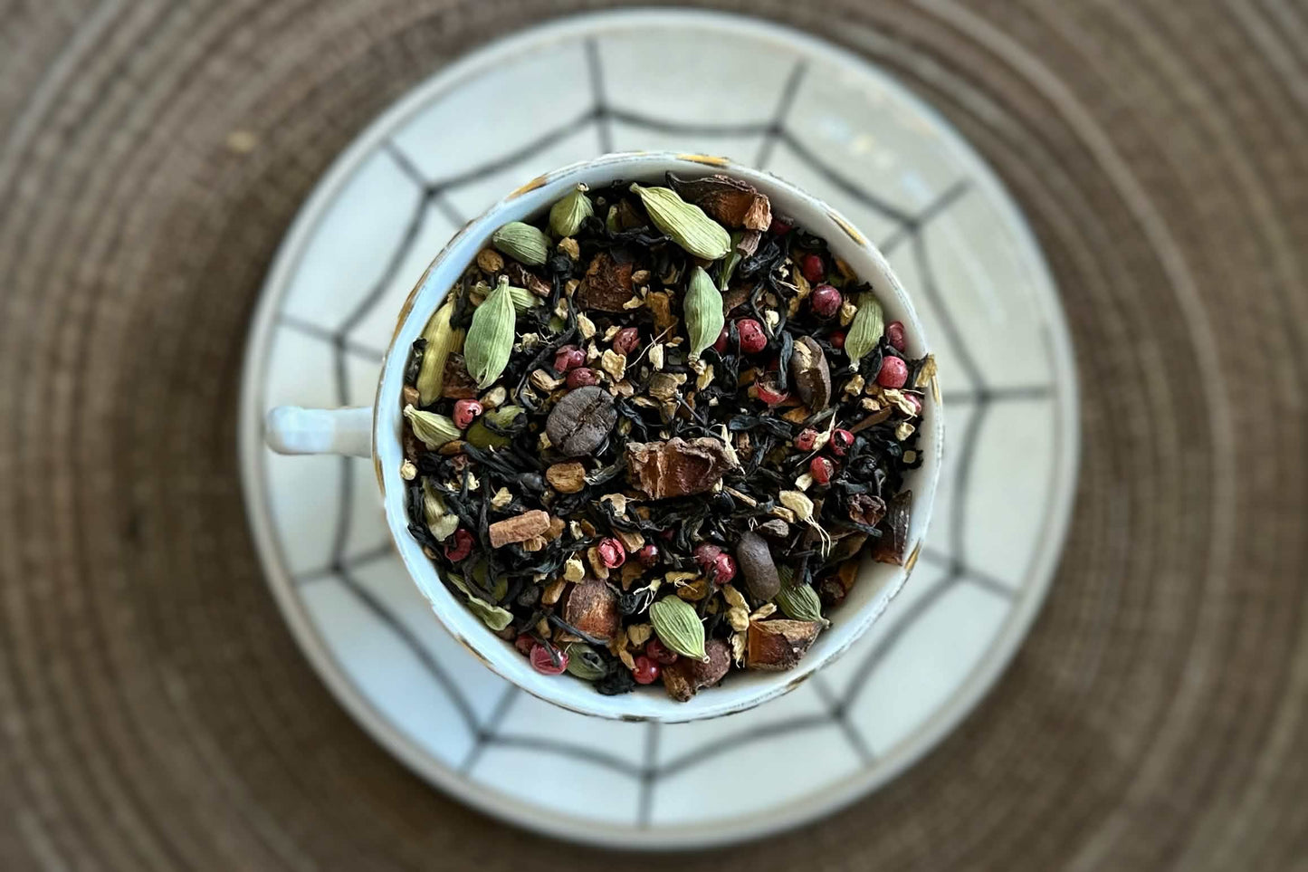 Teacup full of black tea with chai spices and coffee beans on a spiderweb saucer 