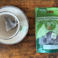 A pyramid teabag in a teacup beside a pouch of teabags