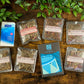 Assorted herbal tea packages on a wooden surface with a mini pack of tissues and a bar of chocolate 