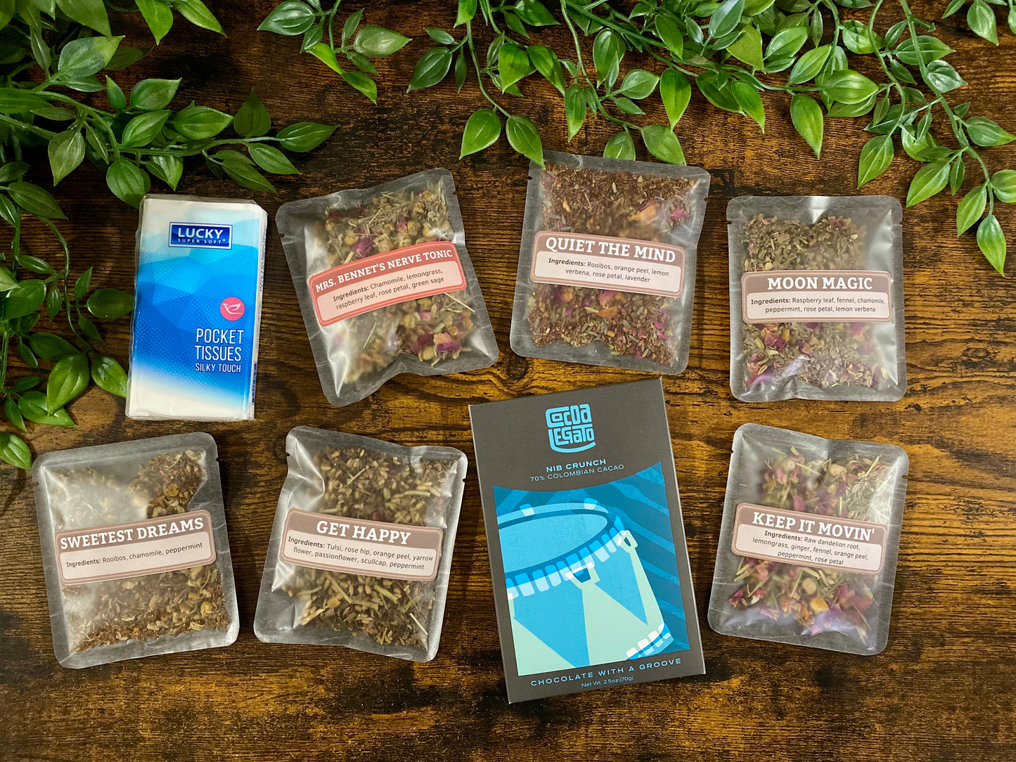 Assorted herbal tea packages on a wooden surface with a mini pack of tissues and a bar of chocolate 