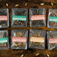 Eight packets of loose leaf chai samples on a wooden table surrounded by cardamom pods