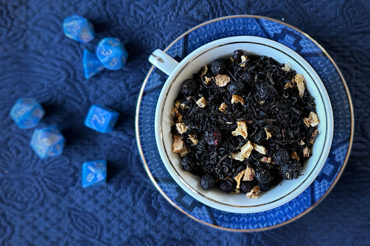 Teacup full of black tea & fruit with dice beside it