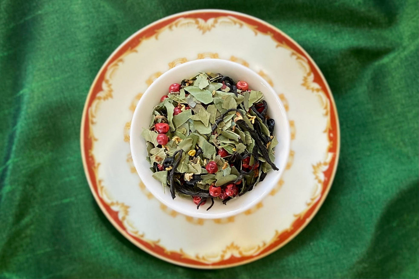 Teacup full of cut green and black leaves with pink peppercorn and tiny yellow flowers