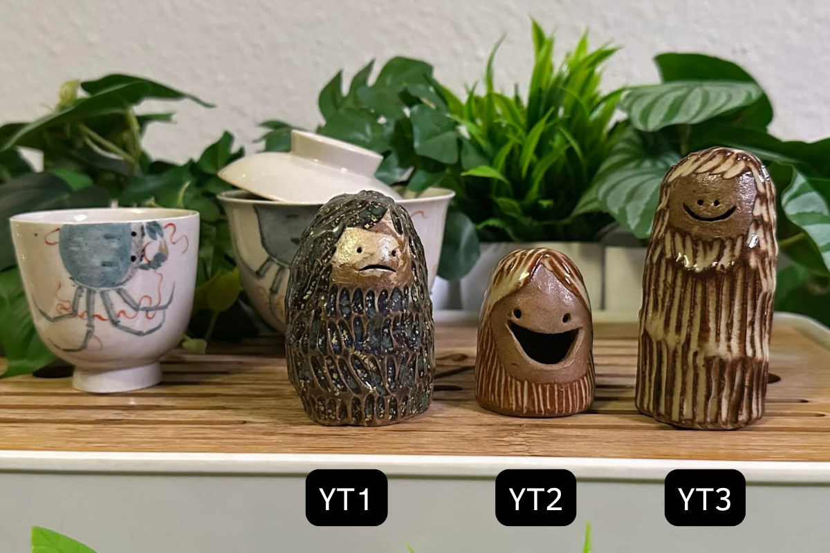 Three yeti tea pets on a gongfu tray: YT1 is dappled dark green and has a gently frowning face. YT2 has the hugest grin you've ever seen and is quite short with curtain bangs. YT3 is very tall and thin with a dopey grin.