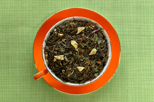 Orange teacup full of roasted green tea, spices and crystalized ginger