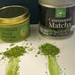 Culinary grade matcha tin beside ceremonial matcha tin. Each has a pile of powder in front of it