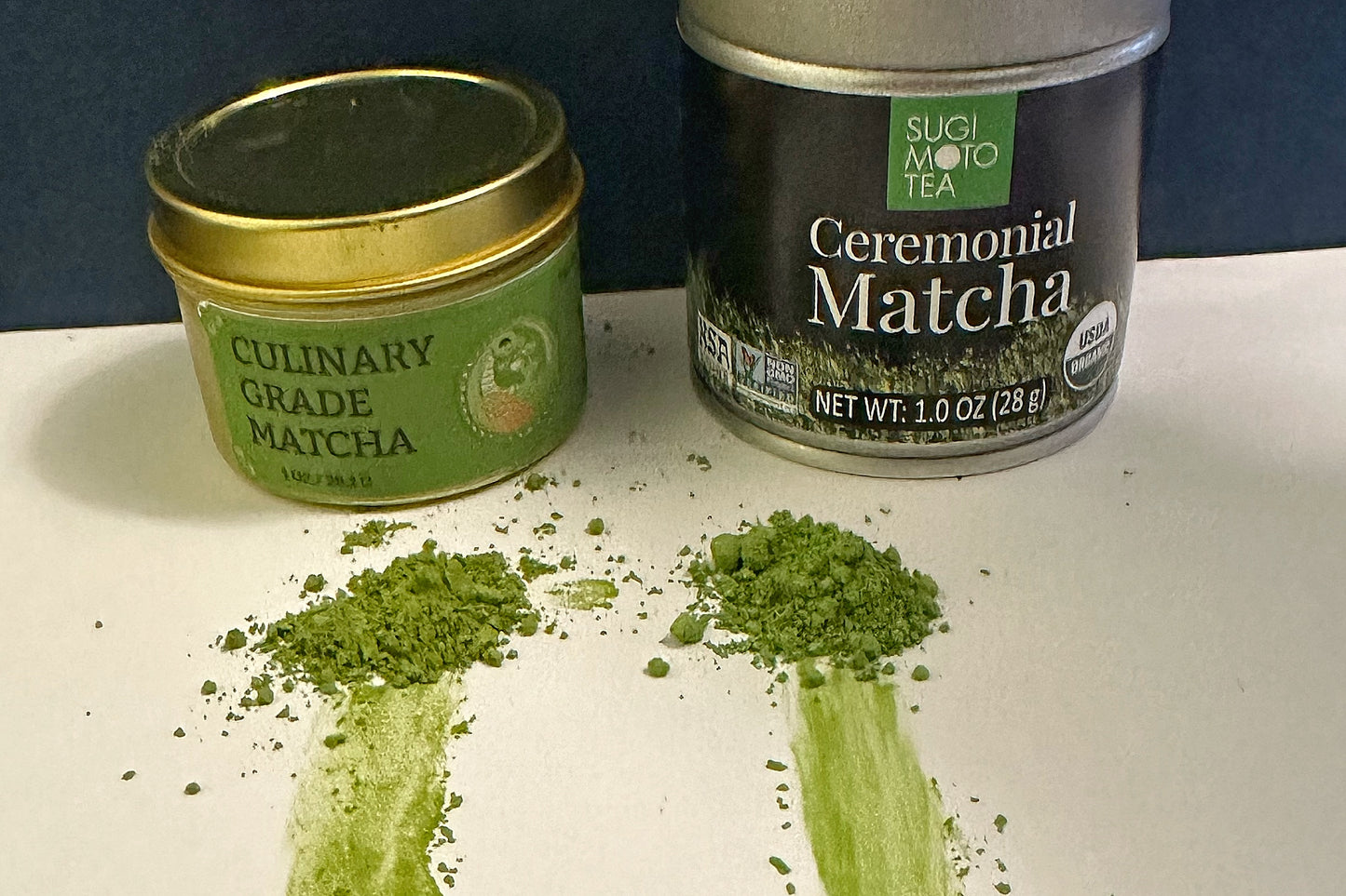 Culinary grade matcha tin beside ceremonial matcha tin. Each has a pile of powder in front of it