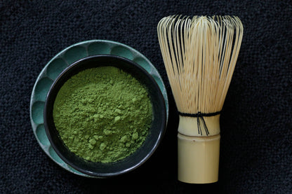 A teacup full of matcha powder beside a bamboo whisk